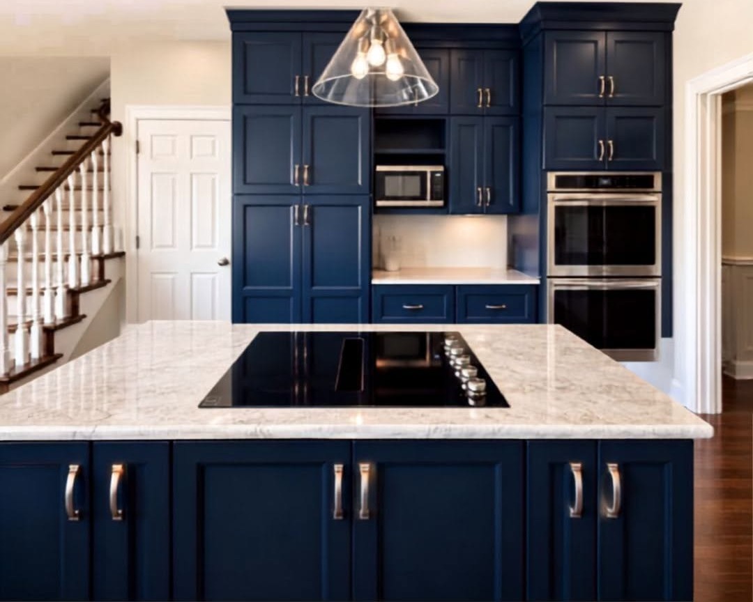 Taj Mahal quartzite island with a cooktop, navy cabinets and stainless wall ovens installed by Absolute Stone Design TN